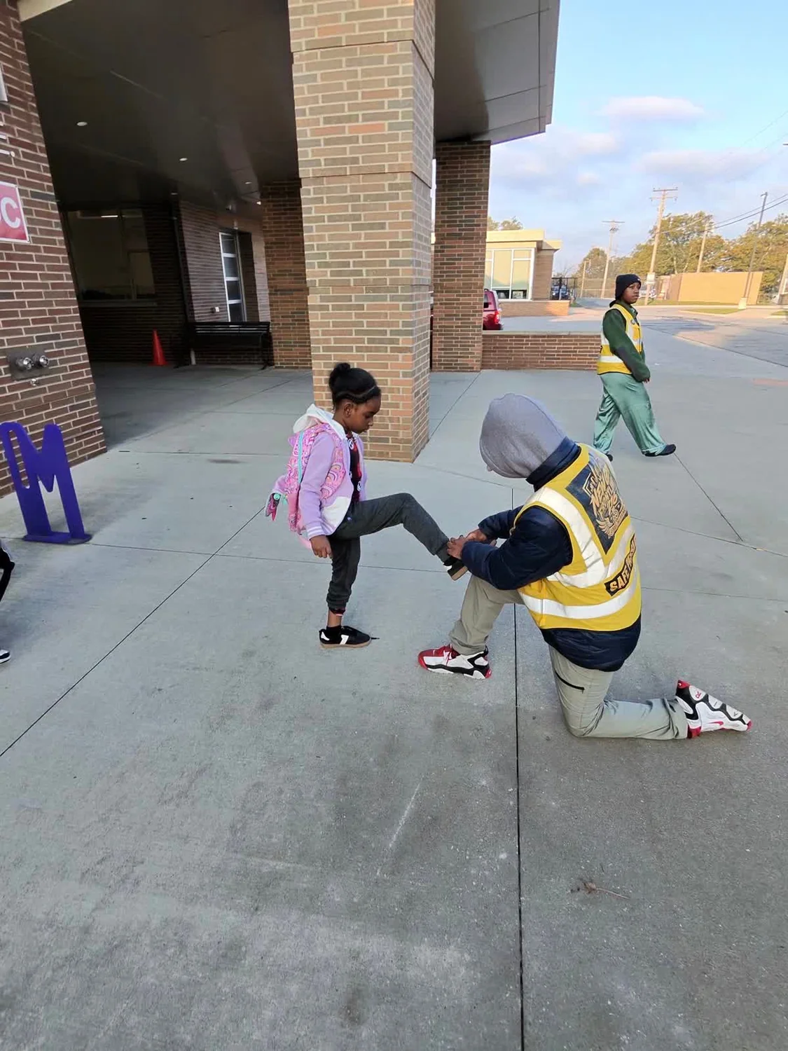 A New Gen team member wearing a branded yellow vest helping a child tie a shoe
