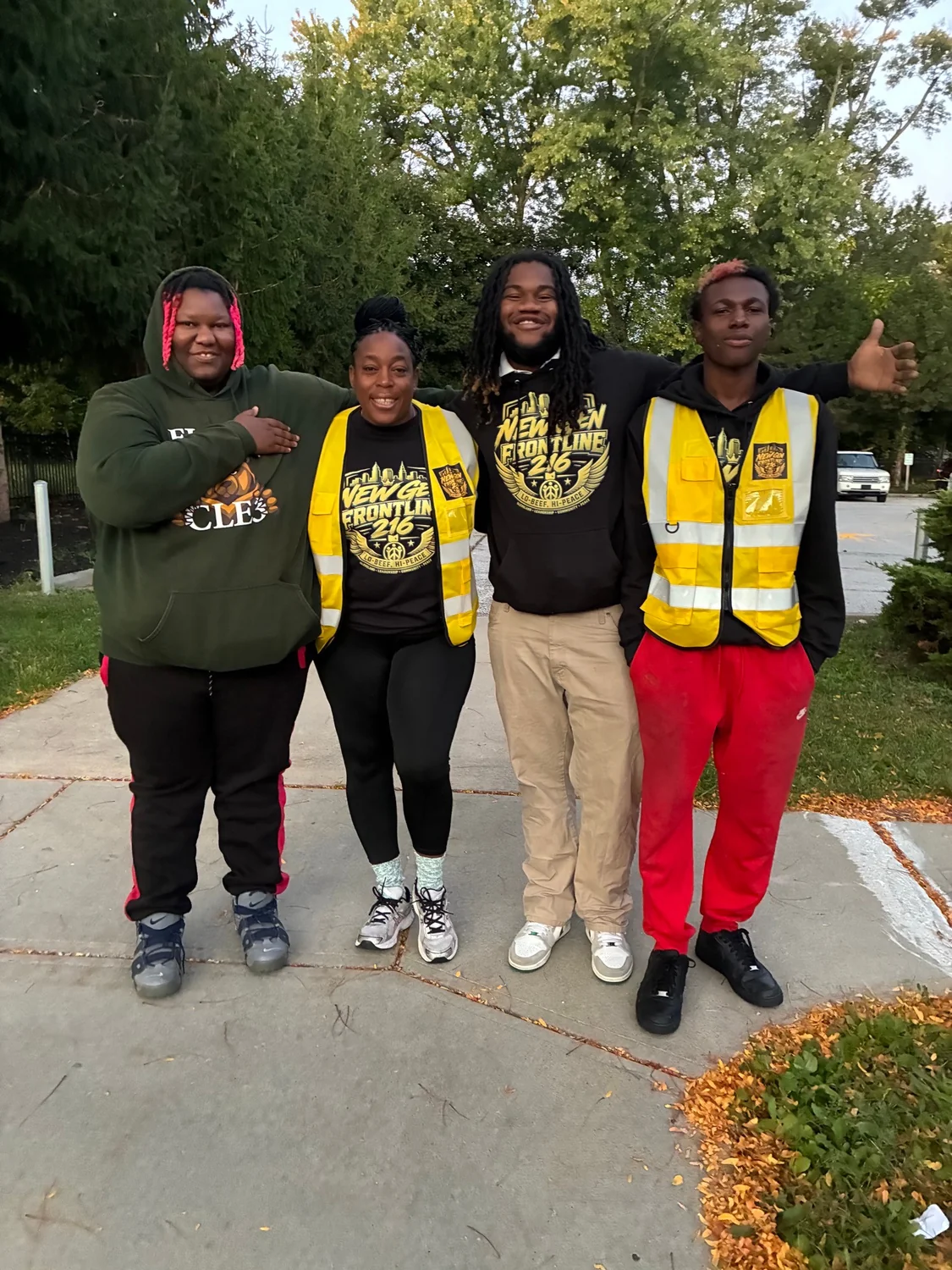 Four young people together outdoors, wearing New Gen shirts and branded yellow vests